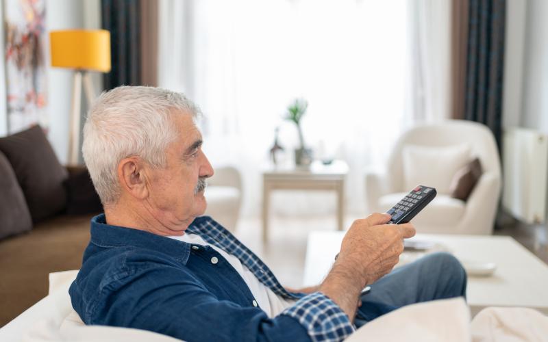 Een senior man zit op zijn bank voor de televisie. Hij heeft een afstandsbediening in zijn hand. Een senior man zit op zijn bank voor de televisie. Hij heeft een afstandsbediening in zijn hand.