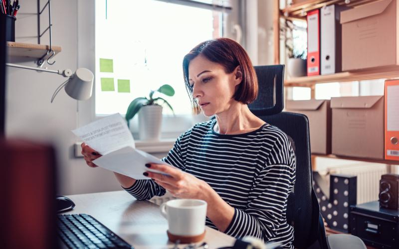 Vrouw met kort rood haar zit achter een bureau en leest een brief Vrouw met kort rood haar zit achter een bureau en leest een brief