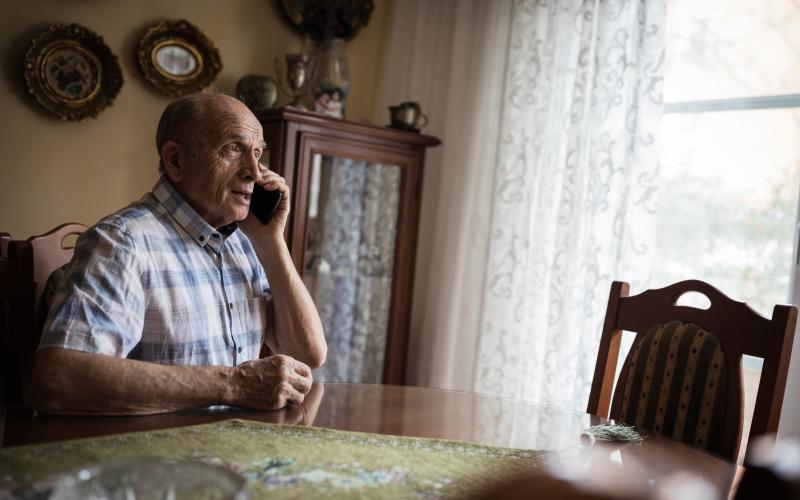 Oudere man zit aan zijn tafel en is aan het bellen Oudere man zit aan zijn tafel en is aan het bellen