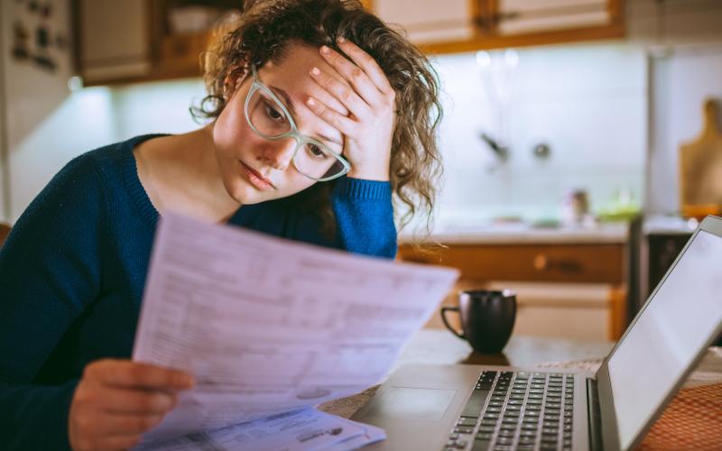 Vrouw zit achter de laptop en kijkt bezorgd naar een brief in haar handen Vrouw zit achter de laptop en kijkt bezorgd naar een brief in haar handen